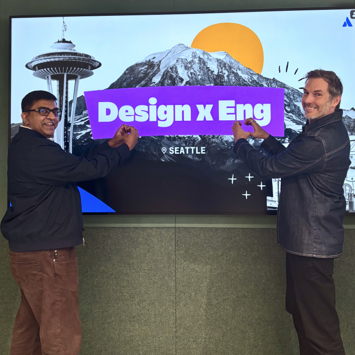 Charlie Sutton, Chief Design Officer, and Rajeev Ravan, Chief Technology Officer, grinning in front of a sign saying "Design x Eng - Seattle"